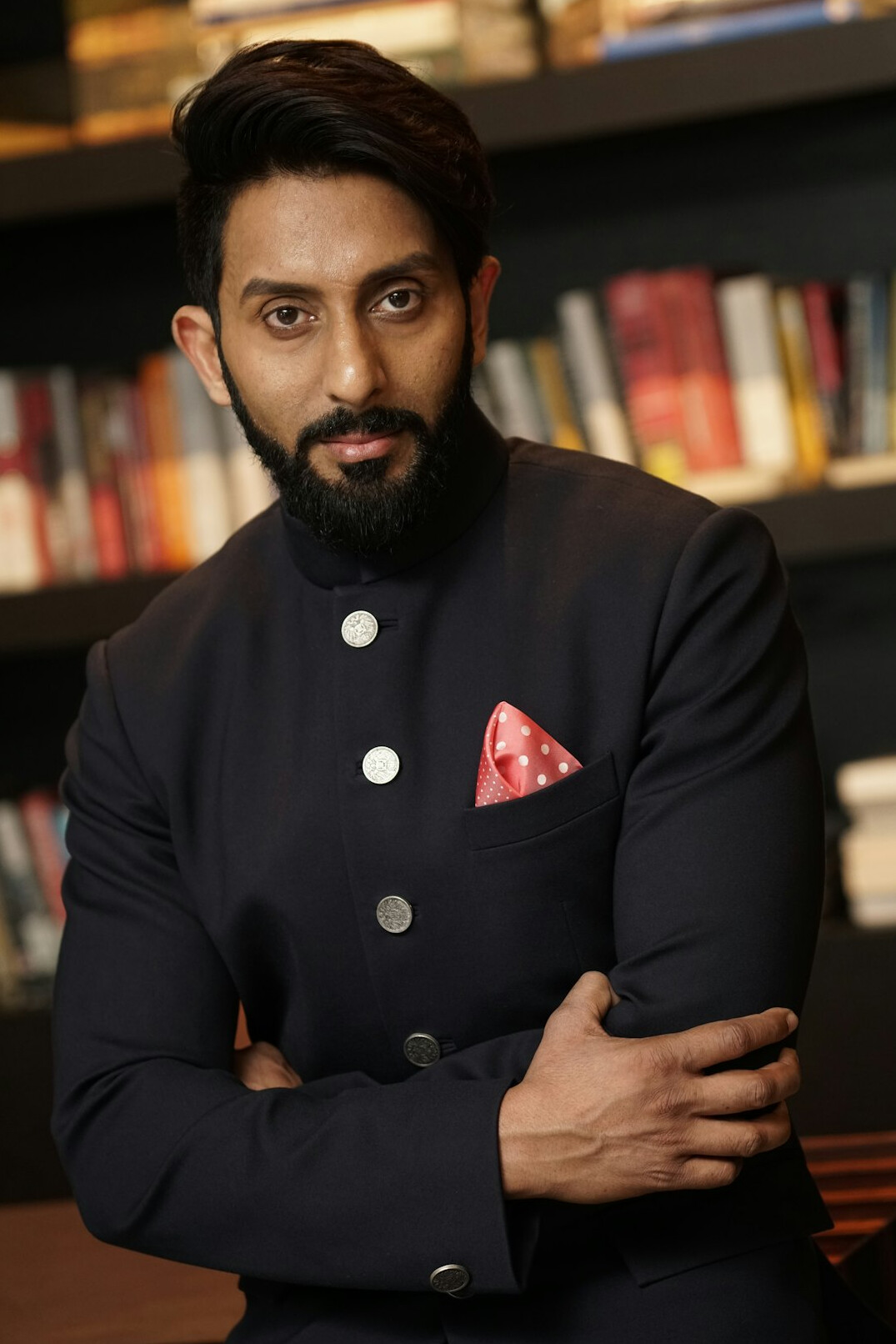 Studio portrait of a man with short dark hair and a beard in a navy blazer